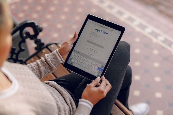 Over the shoulder photo of a female on a bench seat logging in to the mySAWater portal on a tablet.